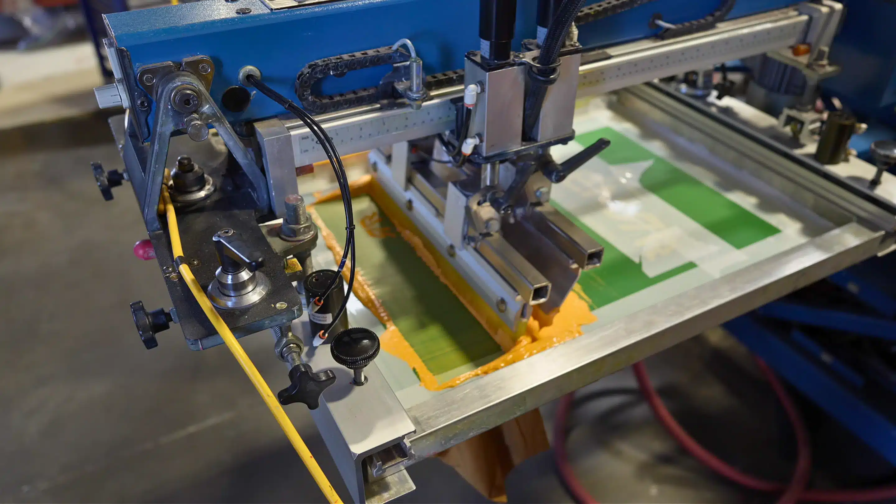 An automatic screen printing press laying down green ink on a t-shirt at Alive Print Shop in Las Vegas.